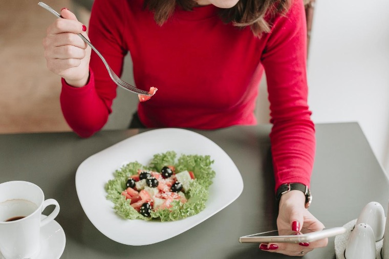 Mujer comiendo y mirando un smartphone